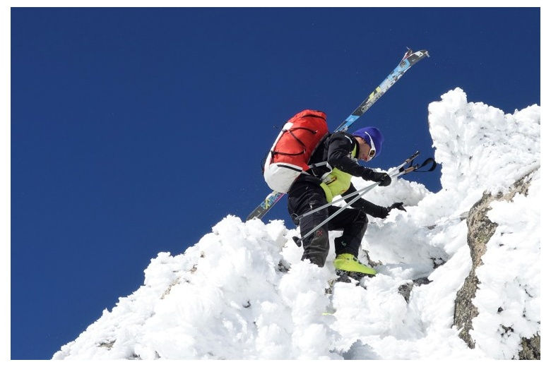 skier climbing up on snowy rocks on a beautiful day